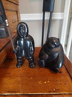 Photo of vintage black cultured stone Inuit and bear sculptures on wooden table, showing full figures