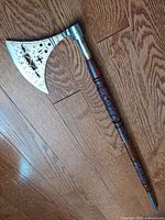 Closer view of the steel axe blade showing the intricate cut-out and scroll work design and carved wooden shaft.