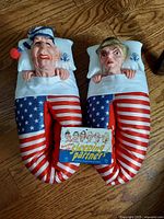 Photo showing both slippers side by side on wood floor with pillow heads, nightcap on Ronald, American flag blanket body and original packaging card.