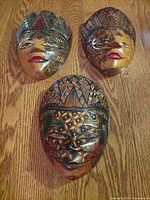 Three wood carved and painted masks laid flat on a wooden surface, displaying intricate patterns and facial features.