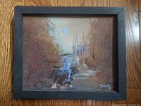 Frontal view of vintage signed oil painting in wood frame on wood floor showing knight on horseback in moonlit setting