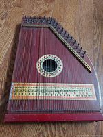 Full front view of the vintage Oscar Schmidt autoharp showing the wooden body, metal strings, decorative rosette around soundhole, and chord scale chart.