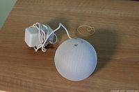 Amazon Echo Dot 4th Generation smart speaker in glacier white with power adapter and USB charger on a wooden surface, showing spherical shape and fabric mesh.