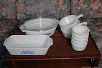 Cookware set on table including 2 casserole dishes with blue floral emblem, 5 bowls stacked, 4 soup dishes stacked with handles visible.