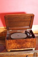 Front view of antique wooden record player with lid open showing turntable and tonearm inside wooden cabinet