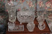 Wide view of all 7 glassware pieces on wood table against floral couch background