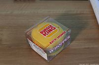 Yellow Burger King bath sponge inside clear plastic cube marked WHOPPER and Burger King logo visible on sponge