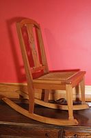 Full side view of child's wooden rocking chair showing the curved rockers and carved backrest.