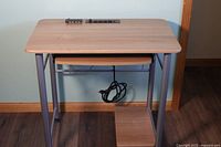 Front view of the small computer desk showing the light wood top, metal legs, and built-in power strip with USB ports.