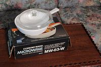 Corning Ware MW-83-W microwave covered browning dish displayed on its original box with clear glass lid on top.