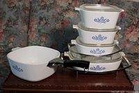 Full view of the Corning Ware cookware pieces stacked and displayed showing lids, sizes, and the detachable handle