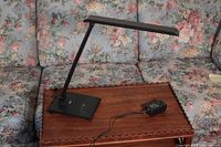 Side view of black LED desk lamp showing adjustable arm, rectangular head, and base with cable and power adapter.