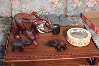 Lot shot showing one large reddish-brown wood elephant, three small black wood elephants, and a round decorative ashtray with elephant engravings