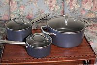 Front view of the Farber Ware pot set arranged on a wooden surface with floral upholstered furniture in the background.