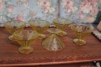 View of all six yellow glass dessert dishes arranged on a wooden surface showing shape and design.