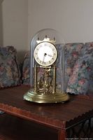 Front view of the brass anniversary clock with white dial and Arabic numerals under glass dome on gold-tone base