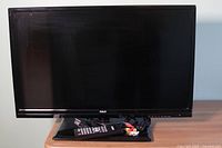 Front view of the RCA 28-inch LED TV with screen and remote plus AV cables placed on stand.