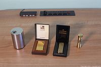 Front view of the four lighters on a wooden surface: Braun metallic lighter, Win lighter in box, Zaima lighter in box, Lord Chester-Field bullet-shaped lighter