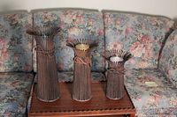 Set of three metal candle holders on a wooden table with floral couch backdrop, showing each holder with a candle in different heights.
