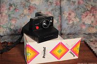 Image of Polaroid Pronto! camera sitting on original box with visible lens and red shutter button.