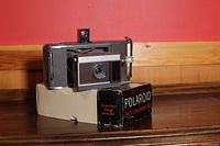 Polaroid Electric Eye model J66 camera sitting on the original box against a red and beige wall.