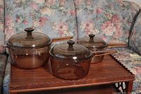 Three amber glass Pyrex pots with matching lids displayed on a wooden tray.