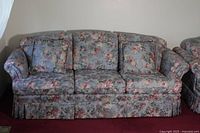 Front view of floral fabric sofa with three seat cushions, floral pattern upholstery, and skirted base.
