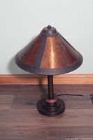 Side view of small table lamp showing copper conical shade with dark metal accents and round base on wooden floor.