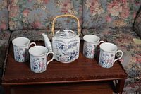 Photo showing tea pot and four matching cups arranged on wooden table against floral upholstery background
