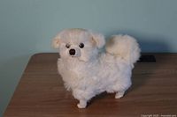Front view of a vintage radio shaped like a white fluffy dog sitting on a wooden surface.