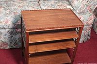 Front view of small walnut shelf showing three horizontal shelves and decorative side panels.