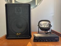 Speaker cabinet showing front metal grille with Squier logo with strobe light and speaker selector to the right on wooden surface.