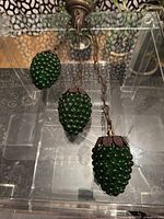 Set of three hanging green glass grape light fixtures resting on clear display box, showing metal caps and chains.
