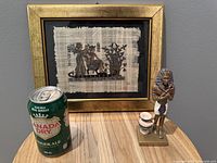 Photo showing the framed Egyptian papyrus artwork next to the Egyptian Pharaoh figurine with two jars and a Canada Dry can for scale.