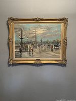 Framed oil painting showing detailed Parisienne scene with lampposts, obelisk, fountains, and pedestrians on a wet street under a clouded sky.