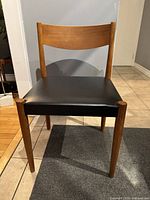 Front view of teak side chair with black vinyl seat cushion on tiled floor.