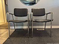 Front view of two chrome tubular steel framed chairs with black vinyl seats and backs, side by side.
