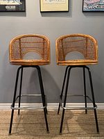 Front view of the two vintage bar stools displaying their caned rattan backs and seats with metal legs.