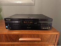 Front view of Pioneer Elite DV-79AVi DVD player showing brand and model, digital display, and control buttons on a wooden surface.