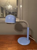 Blue vintage desk lamp on wooden surface, side profile showing adjustable head and base