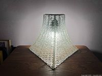 Front-facing view of a pyramid-shaped vintage glass light on a wooden surface, showing the textured glass pattern and central bulb.