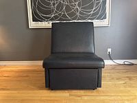 Front view of the convertible chair bed in a compact chair form on a wooden floor with gray walls.