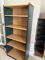 Photo of a wooden book shelf with five shelves, dark green sides, and natural wood top and shelves. The shelf has adjustable holes for repositioning the shelves.