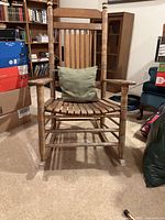 Front view of a wooden rocking chair with slatted seat and green cushion.