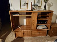 Full view of wood-tone entertainment unit with open shelving and two drawers at the bottom, housing electronics and cables.