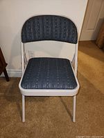 Front view of one white metal frame folding chair with blue upholstery.