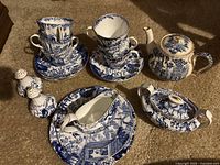 Full set view including tea cups, saucers, teapot, gravy boat with saucer, salt and pepper shakers on carpet background.