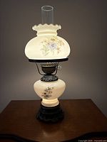 Vintage floral lamp with rounded black base, glass chimney, hand-painted floral pattern on frosted glass shade.