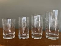 Four vintage glass tumblers of varying heights with etched cornflower designs, showing the smallest to the medium sizes.