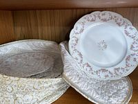 Vintage floral plates with pink flower clusters and scalloped edges stacked on a quilted fabric surface.